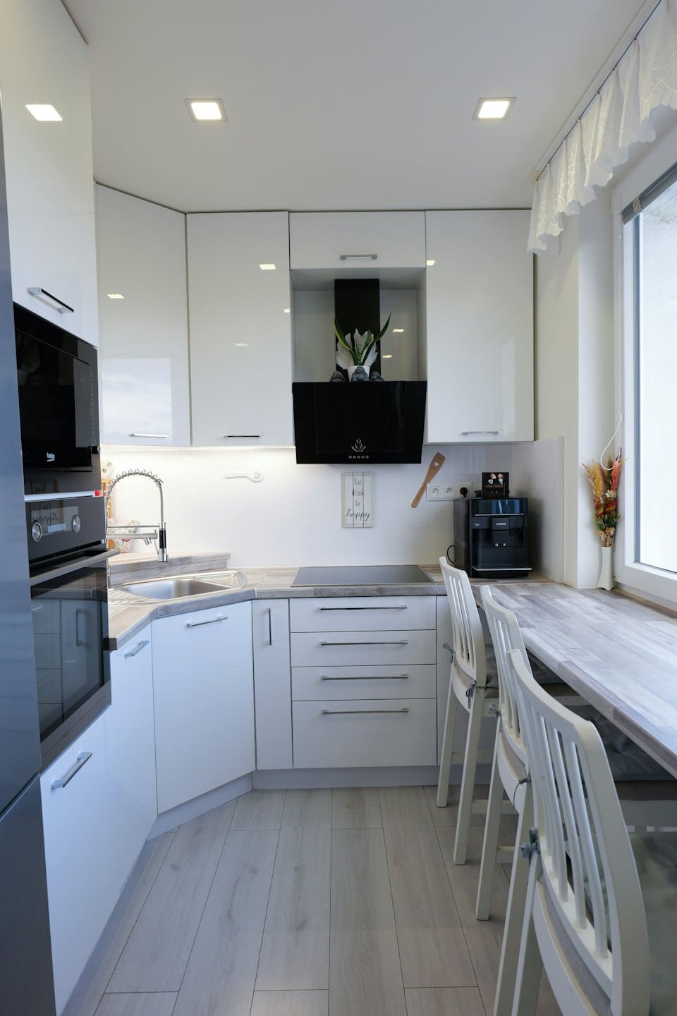 Moderne compacte keuken met witte kasten en houten aanrechtbladen.